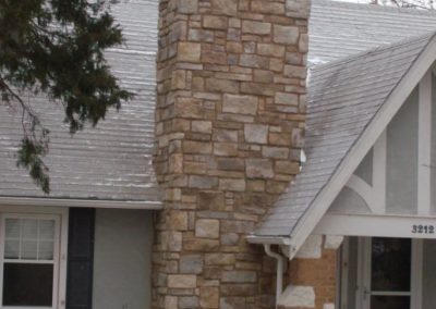 Fully rebuilt stone chimney in front of a grey house with white trim