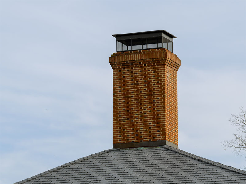 Red brick chimney with black metal chimney cap